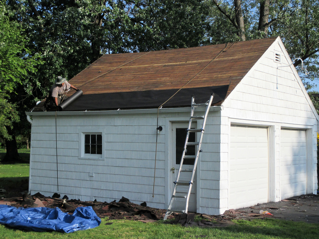 Roofing contractors installing felt underlayment on the garage roof.